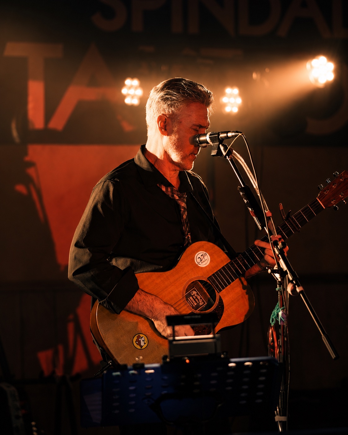 Alex playing acoustic guitar under warm stage lights
