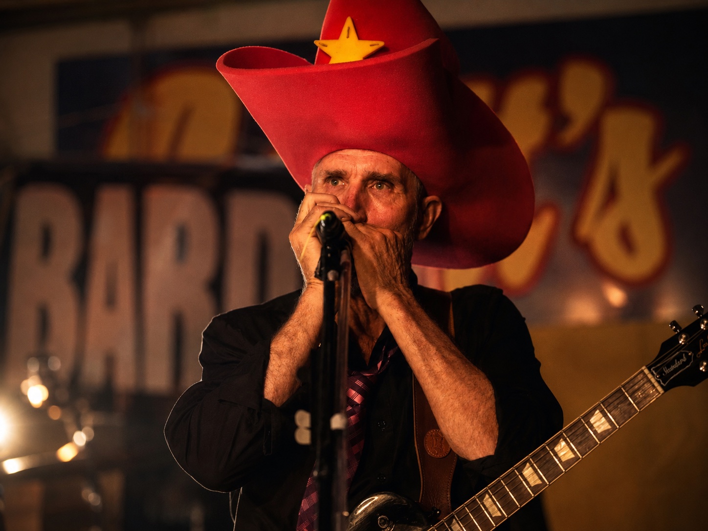 Alex performing harmonica in a red hat